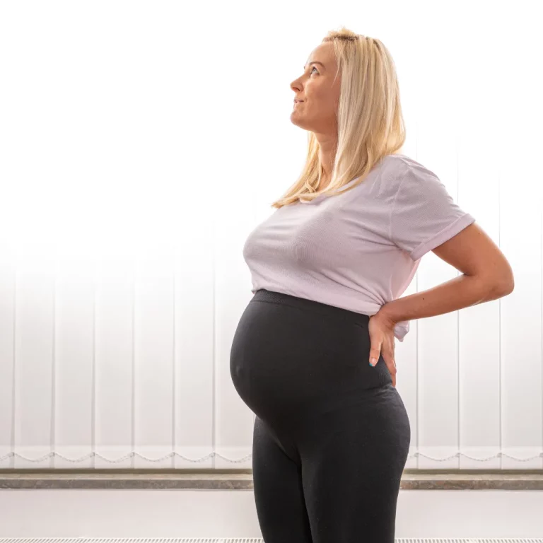 en gravid kvinna i profil som håller händerna på ryggen som stöd